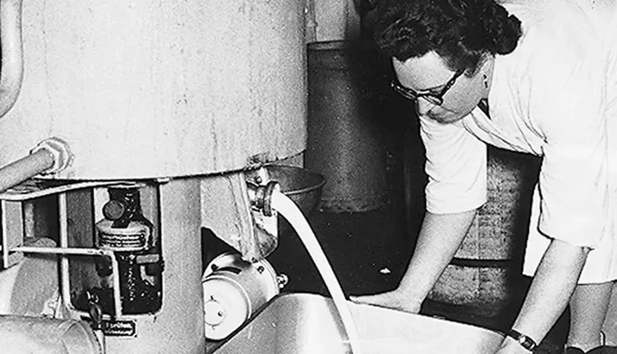 Historische Schwarzweißaufnahme aus den Anfangsjahren von Annemarie Börlind: eine Frau an einer Anlage, aus der eine helle Emulsion fließt