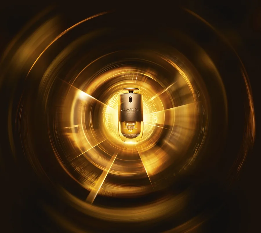Der Flakon von Clarins Double Serum Eye mit Drehdosierer vor einem goldenen Lichtkreis